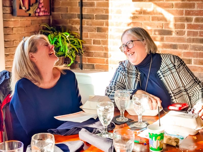 Two females smiling and laughing at a dining table in a brick wall restaurant
